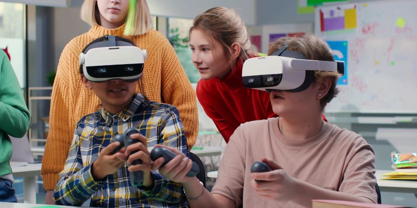 Dos niños con lentes y mandos de realidad virtual mientras sus compañeros los guian desde atrás