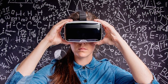 Mujer joven con lentes de realidad virtual delante de una pizarra con ecuaciones matemáticas