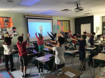 Niños en salón de clase estirando los brazos hacia adelante