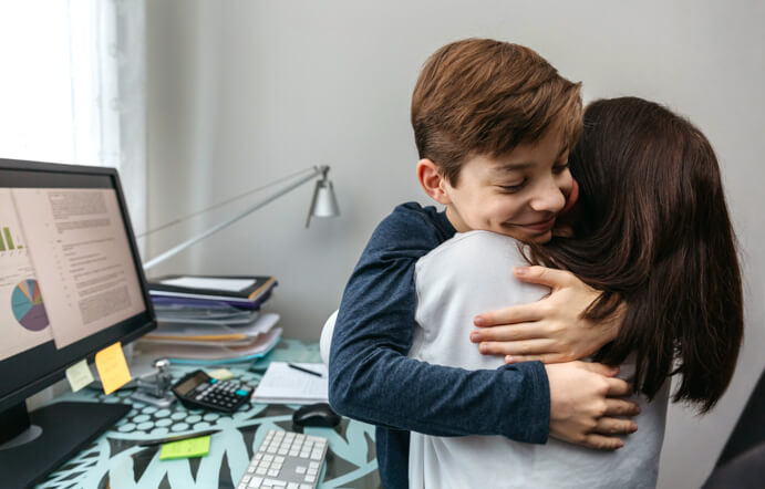 Chico adolescente abrazando con fuerza a su mamá luego de una conversación frente a su escritorio